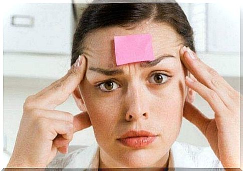 A woman rubs her temples with a sticky note attached to her forehead.