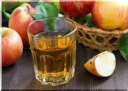 A drink made from apple cider vinegar, which helps against heavy menstrual bleeding, sits on a table in front of some apples.