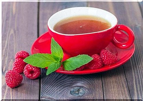 A cup of raspberry tea with some raspberries and raspberry leaves next to it.